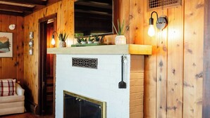 A wooden interior with a fireplace, a mounted television, and a brick-patterned floor. - Island view Crooked Lake cottage, 170' frontage, best views! (Alanson)