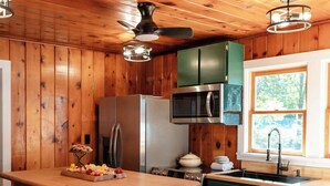 A kitchen with wooden walls, a central island, a refrigerator, a microwave, and a sink. - Island view Crooked Lake cottage, 170' frontage, best views! (Alanson)