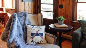 A cozy room with a wooden ceiling, a chair with a blanket, a table with a plant, and a door with a window. - Island view Crooked Lake cottage, 170' frontage, best views! (Alanson)