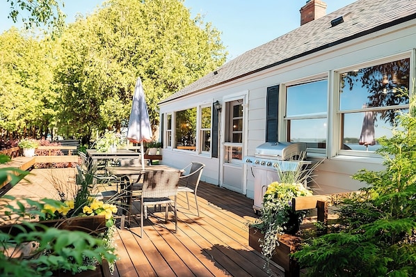 A wooden deck with outdoor furniture, a grill, and a view of a forested area. - Island view Crooked Lake cottage, 170' frontage, best views! (Alanson)