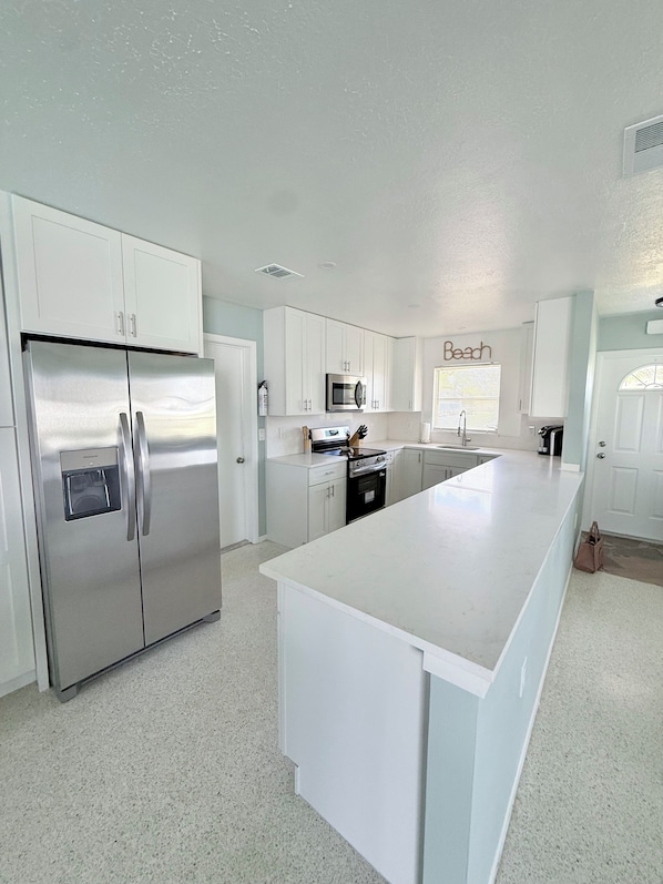 A modern kitchen with white cabinetry, stainless steel appliances, and a large island.