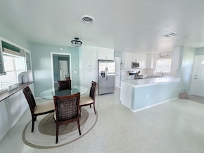 A modern kitchen with white cabinetry, a central island, and a dining area with a glass table and wicker chairs.