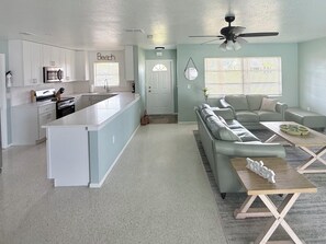 A modern kitchen with white cabinets, a central island, and a dining area with a sofa and coffee table.