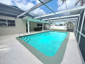Une piscine entourée de parois en verre, un espace patio aménagé avec du mobilier d’extérieur et une vue sur des palmiers.