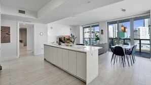 Uma cozinha moderna com uma ilha central, área de jantar com cadeiras e grandes janelas com vista para a cidade.