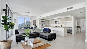 Uma sala de estar moderna com um sofá seccional preto, uma mesa de centro de vidro e vista para a cidade.