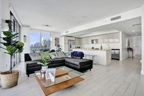 Ein modernes Wohnzimmer mit einem schwarzen Ecksofa, einem Glastisch und Blick auf die Stadt.