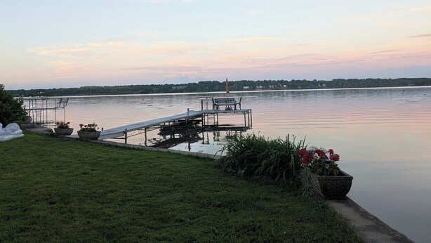 A lakeside dock with a grassy area and potted plants. - Lake House getaway!!! 2-bedroom Cayuga Lake, lake front property! (Seneca Falls)