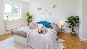 Ein Schlafzimmer mit Bett, Nachttischen, einem Fenster und einer Topfpflanze.