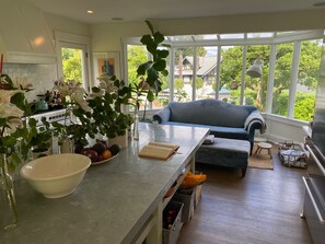 A modern kitchen with a large island, a dining area with a blue sofa, and a view of houses through large windows. - World Cup Headquarters! Perfect for large groups! (Seattle)