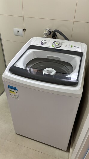A front-loading washing machine with a control panel, a water inlet, and a drain hose. - Ravello Residential AP01 Foz do Iguaçu (Foz do Iguaçu)