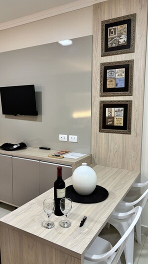 A modern kitchen with a wooden countertop, a wine bottle, and glasses. There is a TV mounted on the wall and a framed collage of vintage beer labels. - Ravello Residential AP01 Foz do Iguaçu (Foz do Iguaçu)