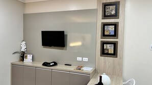 A hotel reception area with a flat-screen TV mounted on the wall, a wooden cabinet below, and three framed pictures on the wall. - Ravello Residential AP01 Foz do Iguaçu (Foz do Iguaçu)