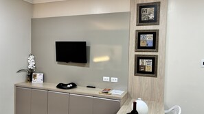 A hotel reception area with a flat-screen TV mounted on the wall, a wooden cabinet below, and three framed pictures on the wall. - Ravello Residential AP01 Foz do Iguaçu (Foz do Iguaçu)