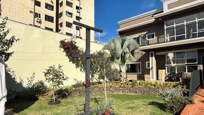 A courtyard with a cross-shaped planter, a palm tree, and a building with a balcony. - Ravello Residential AP01 Foz do Iguaçu (Foz do Iguaçu)