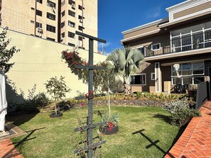 A courtyard with a cross-shaped planter, a palm tree, and a building with a balcony. - Ravello Residential AP01 Foz do Iguaçu (Foz do Iguaçu)