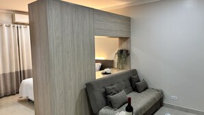 A modern hotel room with a large mirror, a sofa, and a bedside table with a bottle and glasses. - Ravello Residential AP01 Foz do Iguaçu (Foz do Iguaçu)
