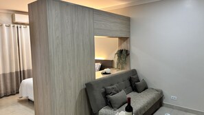 A modern hotel room with a large mirror, a sofa, and a bedside table with a bottle and glasses. - Ravello Residential AP01 Foz do Iguaçu (Foz do Iguaçu)