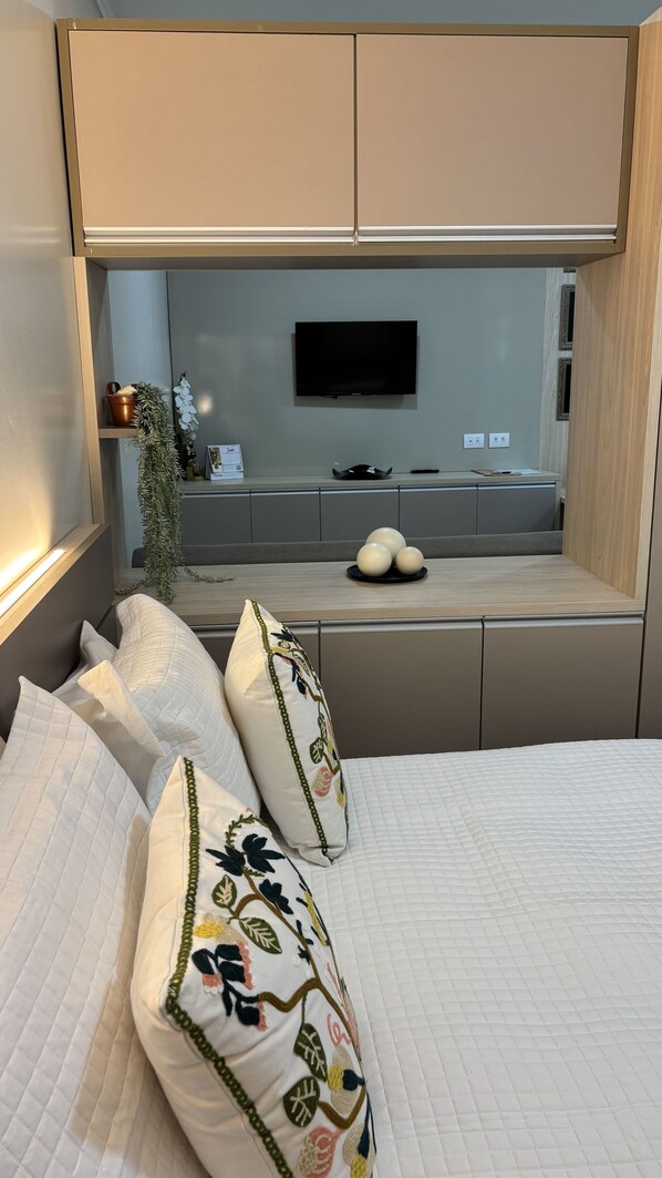 A bedroom with a bed, pillows, a TV, and a small kitchenette area. - Ravello Residential AP01 Foz do Iguaçu (Foz do Iguaçu)