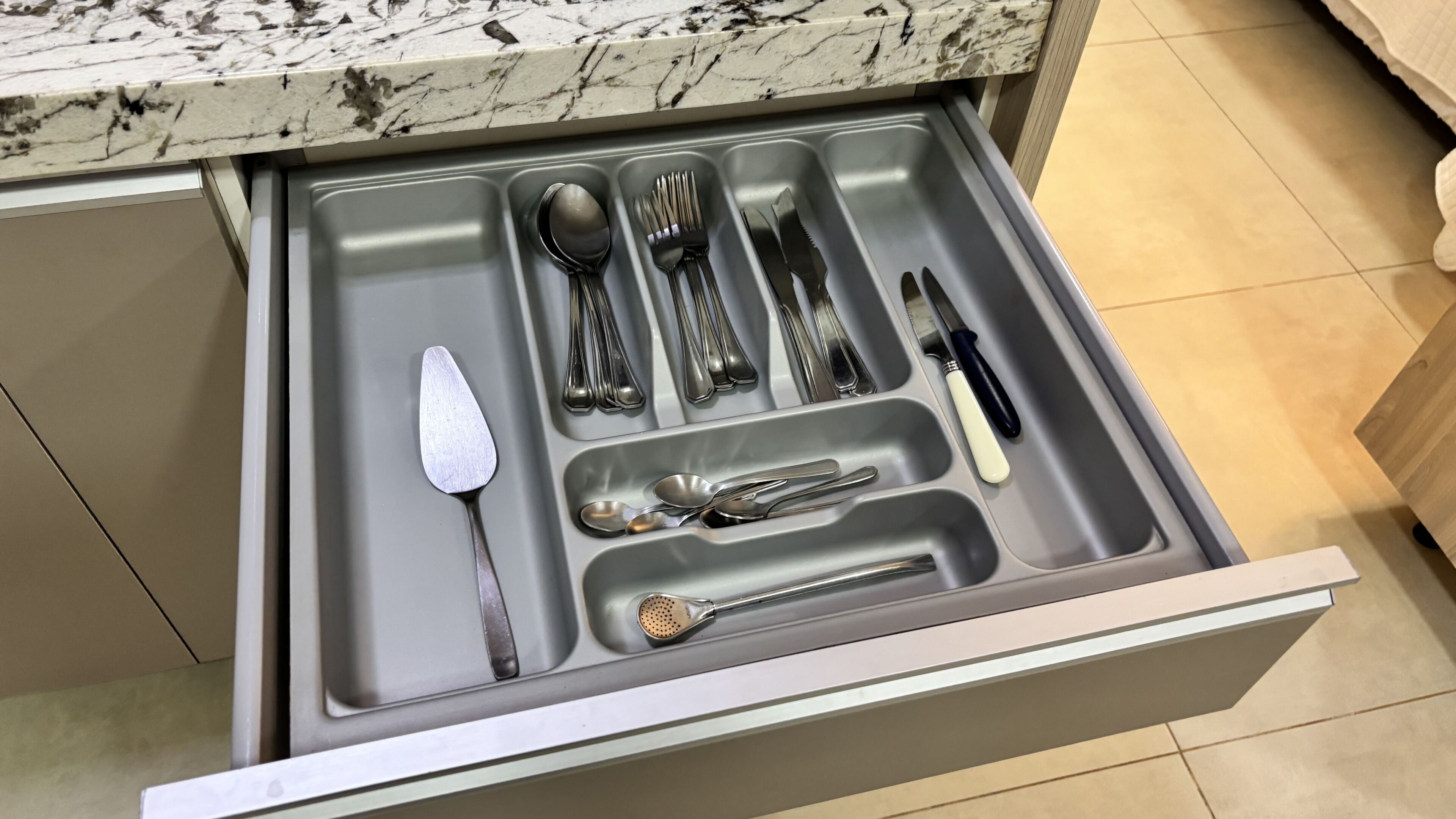 Un cajón con diversos utensilios de cocina, como cucharas, tenedores, cuchillos y una espumadera.