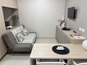 A modern living room with a sofa, a dining table, a TV mounted on the wall, and a small cabinet. - Ravello Residential AP01 Foz do Iguaçu (Foz do Iguaçu)