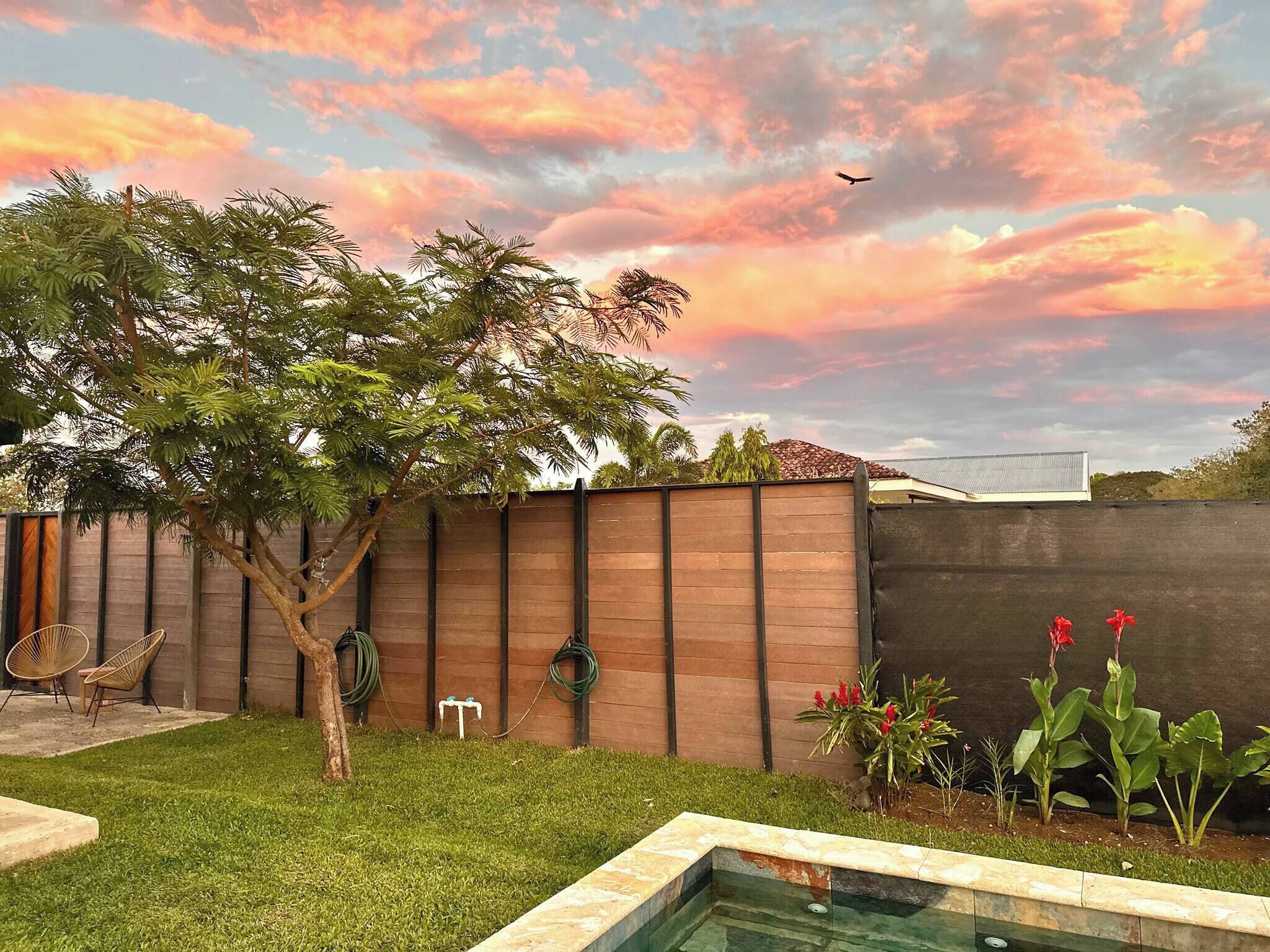 Un patio trasero con piscina, valla de madera y un árbol.