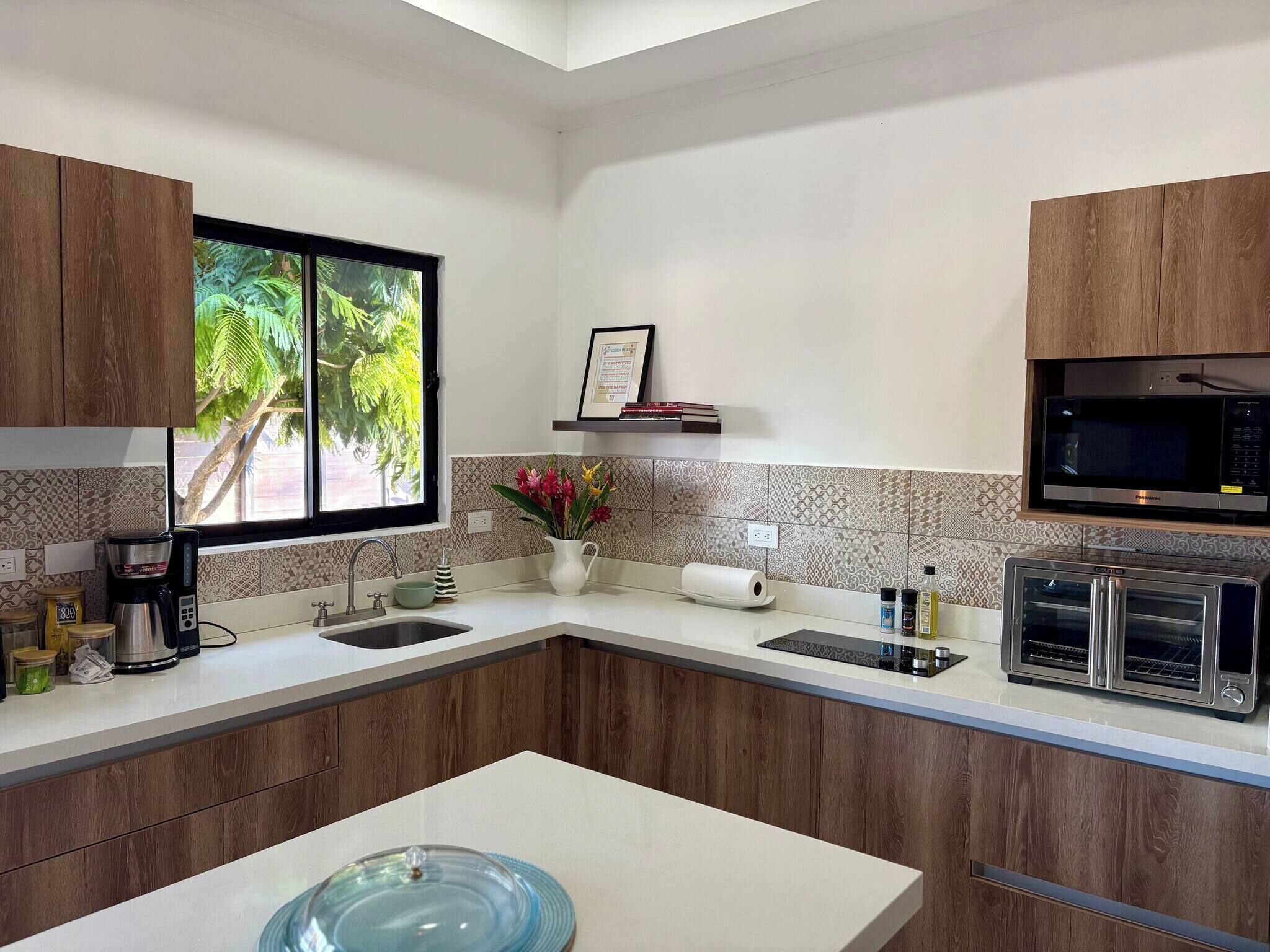 Une cuisine moderne avec des meubles en bois, un four à micro-ondes encastré, un four grille-pain et une fenêtre donnant sur un espace verdoyant.