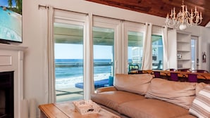 Una sala de estar con un amplio ventanal con vista al océano, un candelabro y un techo de madera.