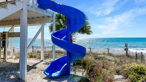 Un tobogán azul en espiral en un lugar junto a la playa, con una estructura de madera y vista al océano.