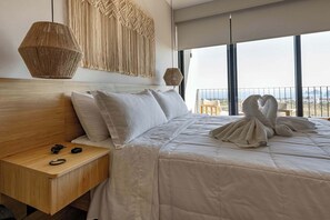 Ett hotellrum med en stor säng, ett nattduksbord i trä, en väggdekoration i makramé och utsikt över havet genom stora fönster.