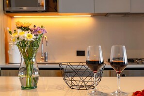 Eine Küche mit einem Blumenstrauß in einer Vase, zwei Weingläsern und einem geometrischen Drahtkorb auf einem Tisch.