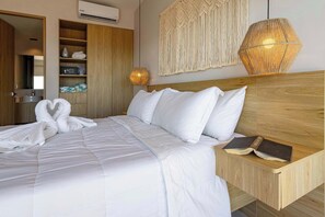 Ein ordentlich gemachtes Bett mit weißen Leinen, einem Holz-Kopfstück und einem Nachttisch mit einem Buch.