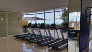 Une salle de sport équipée de tapis de course, une porte en verre portant l’inscription « SORTIE », et une vue sur le paysage urbain.