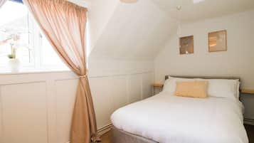 Une chambre à coucher avec un lit, une fenêtre avec des rideaux, une table de chevet et des œuvres d’art accrochées au mur.