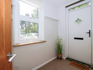 A hallway with a wooden door, a white door with a window, a small potted plant, and a doormat. - Corner House (Shrewsbury)