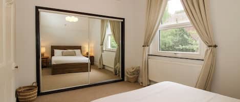 A bedroom with a large mirror, a bed, a window with curtains, and a radiator.