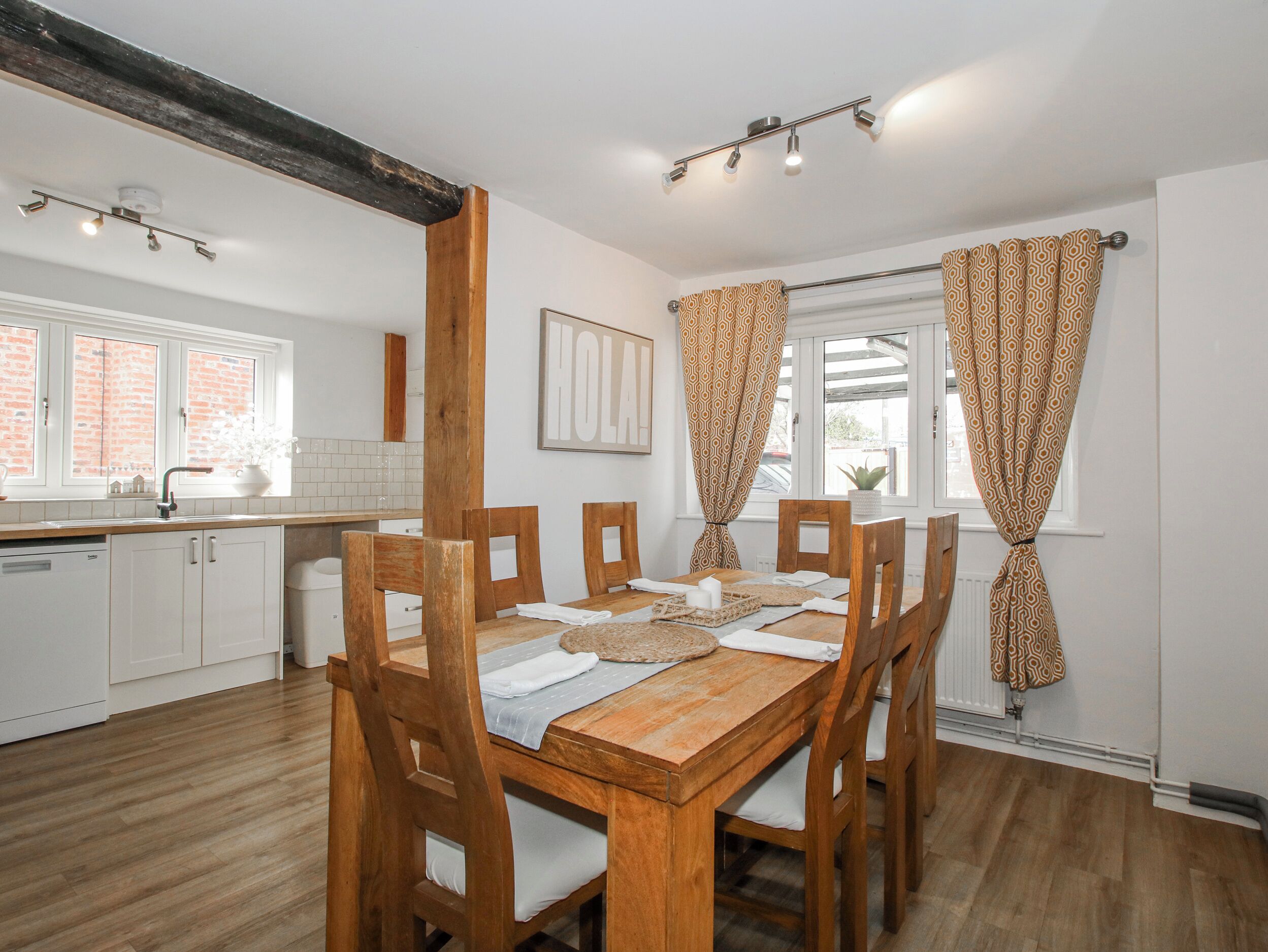 Un comedor con mesa y sillas de madera, una cocina con armarios blancos y cortinas estampadas.