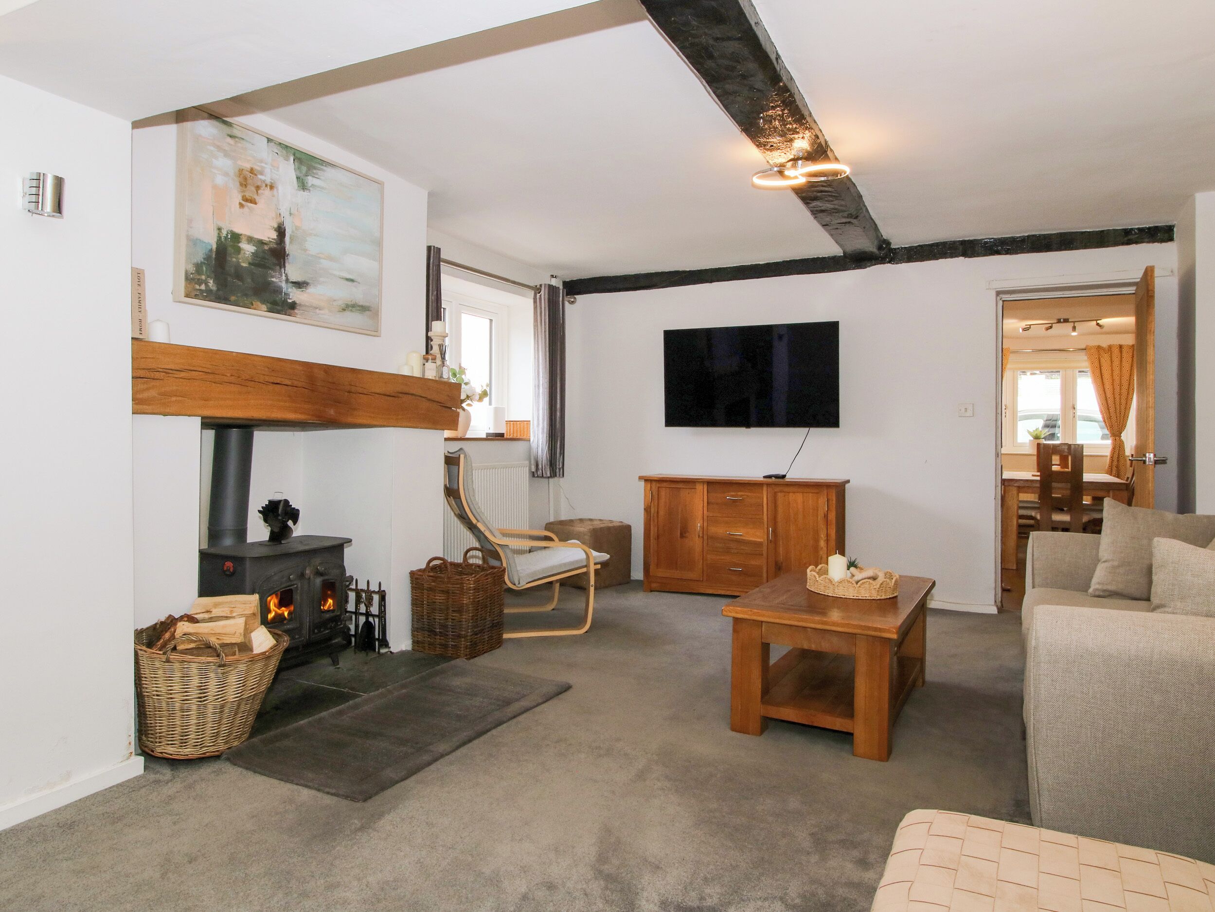 A cozy living room with a fireplace, a television mounted on the wall, and a dining area visible through an open door.