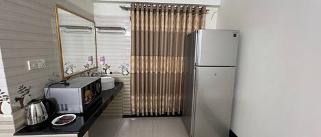 A compact kitchen with a refrigerator, a sink, and a mirror.