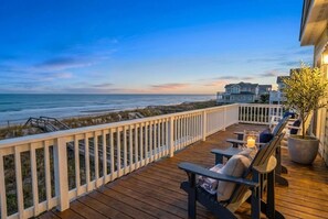 Eine Holzterrasse mit Sitzgelegenheiten im Freien, mit Blick auf einen Strand und den Ozean.