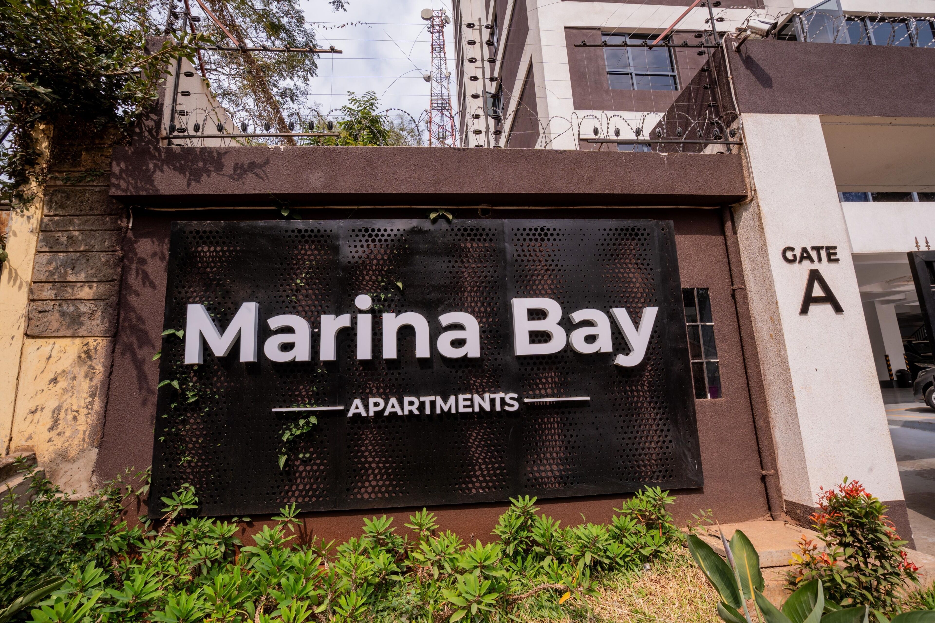 Ein Schild mit der Aufschrift 'Marina Bay Apartments', ein Tor mit dem Buchstaben 'A' und ein Gebäude im Hintergrund.