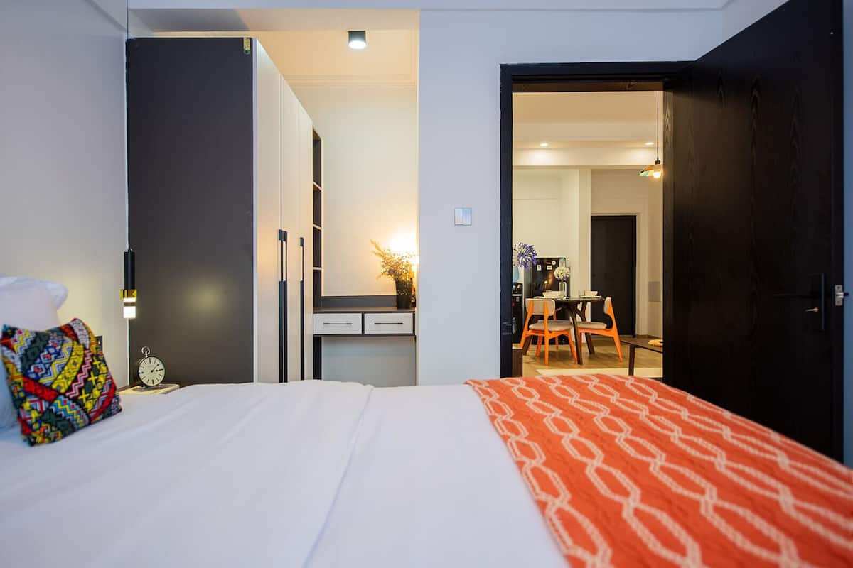 A hotel room with a bed, a bedside table, a chair, a desk, and a door leading to a bathroom.