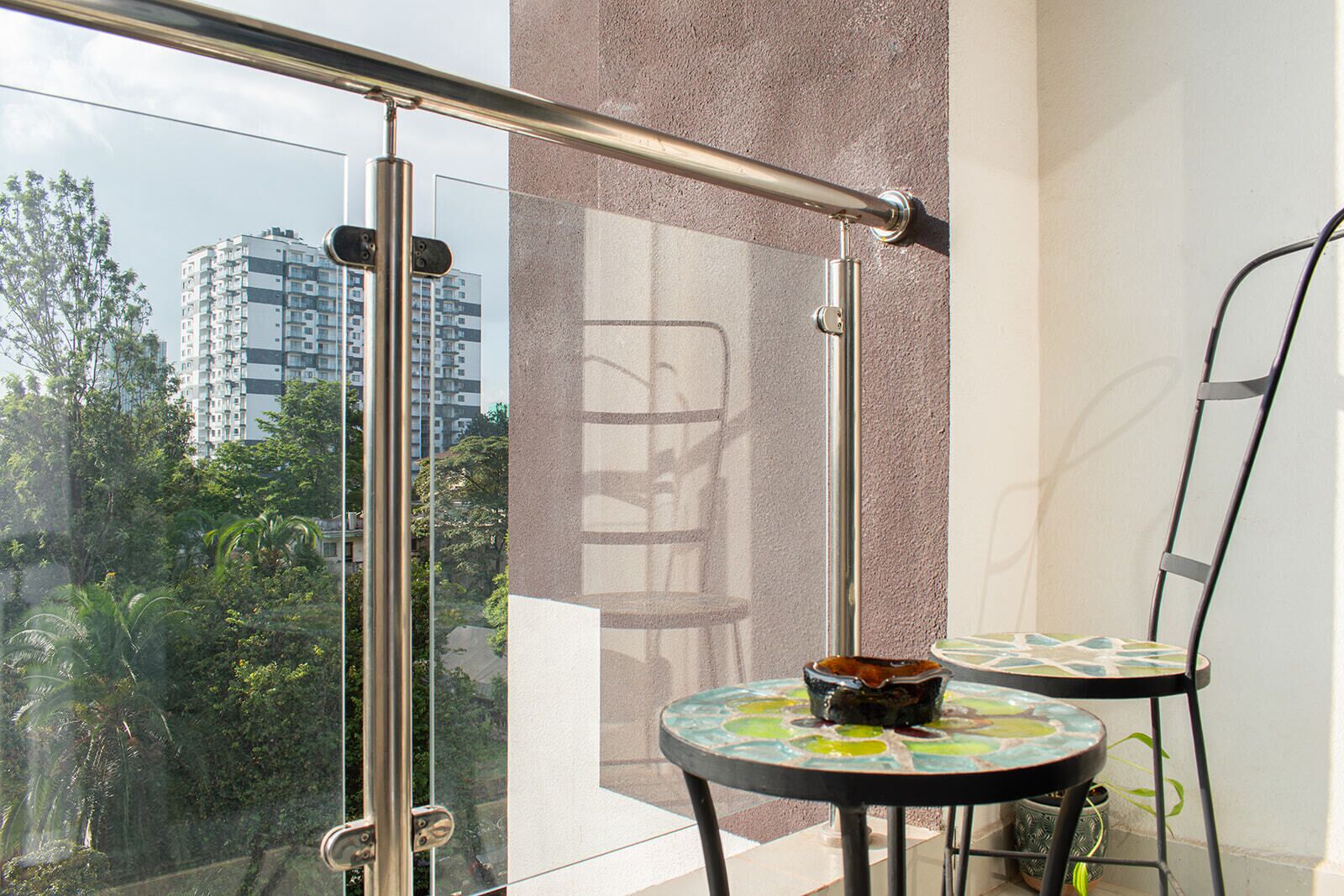 Ein Balkon mit Glastür, Metallgeländer, einem kleinen Tisch und einer dekorativen Schale sowie einem Stuhl.