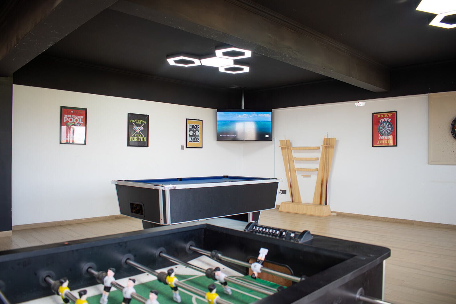 Una habitación con mesa de futbolín, mesa de billar, dardos y televisor en la pared.