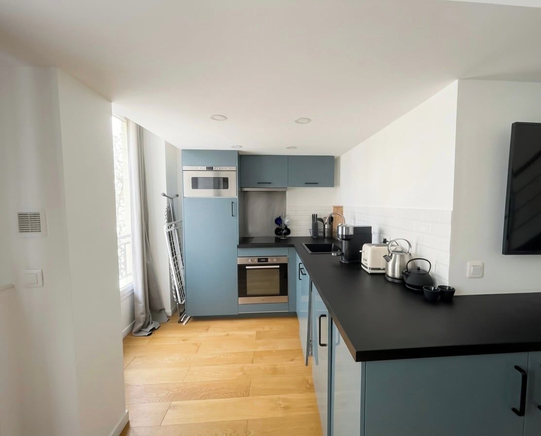 A modern kitchen with blue cabinets, a black countertop, and stainless steel appliances.