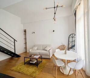 Ein modernes Wohnzimmer mit Treppe, einer Couch, einem Esstisch mit Stühlen und einer Pendelleuchte.