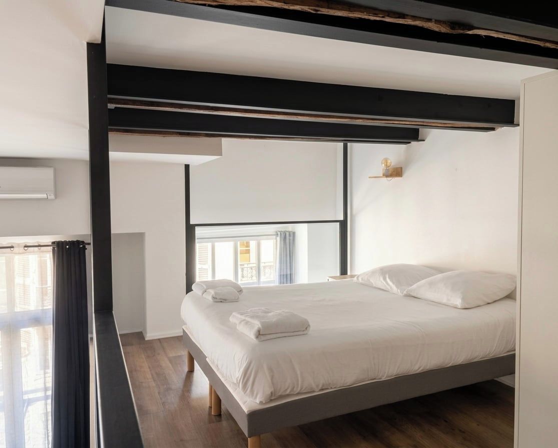 A modern bedroom with a bed, a window, and a black ceiling beam.