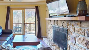 Ein Wohnzimmer mit Kamin aus Stein, einem Flachbildfernseher, einem Deckenventilator und Blick ins Freie.