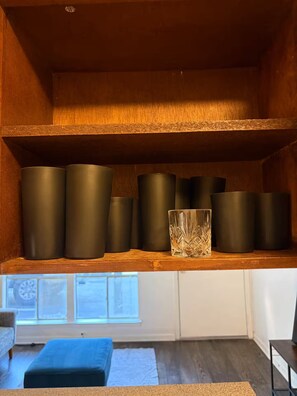 A room with a wooden shelf holding several cylindrical containers, a glass vase, and a patterned rug on the floor. - Delightful Cozy 1x1 by the Drag (Austin)