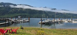Un port de plaisance avec des bateaux amarrés, une jetée en bois et une zone herbeuse avec des chaises rouges.
